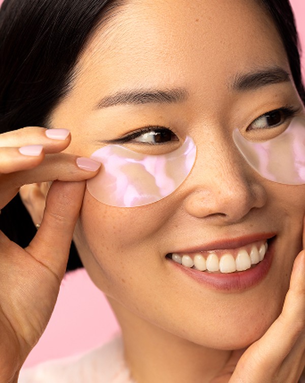 Woman smiling while applying Brighten Up under-eye patches